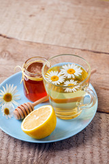 Herbal tea in a glass bowl with camomile flowers, lemon and honey on rustic wooden background, selective focus