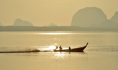 A fishing boat silhouette is sailing on a sparkle gold lake surface in a morning