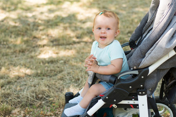 Adorable little girl in bright stylish clothes sitting in pushchair outdoors . Autumn walks with kids