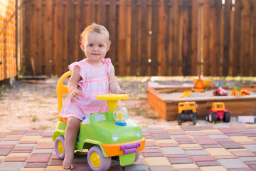 Fototapeta premium Baby girl driving a toy car at the playground outdoor, summer background, copy space