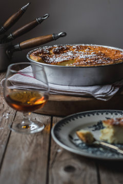 Cottage cheese baked pudding served on plate and glass of cognac on towel against wooden table