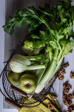 From above metal basket with apples, celery, fennel bulbs and walnuts arranged on board against white background