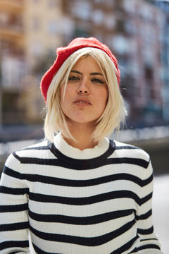 Young blonde woman in striped black and white shirt and red French cap on blurred background