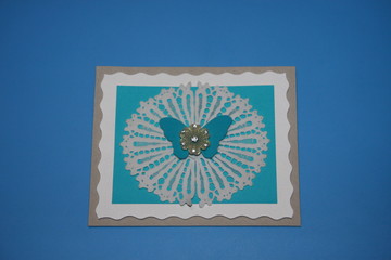 blue greeting card with a lace and butterfly pattern and a wavy border with a flower and rhinestones