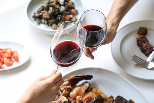 From Above Crop Hands Of People Clinking With Wine Glasses While Eating Delicious Meal On White Background