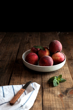 Appetizing bright peaches with leaves in white plate on wooden table and knife on cloth napkin
