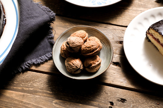 From above strong ripe walnuts in bowl linen napkin and cake in plate on wooden table
