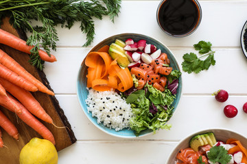 From above bowl of yummy boiled rice with various fresh vegetables placed on white tabletop near soy sauce