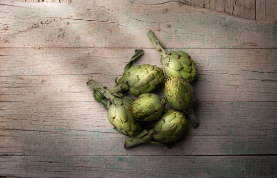 Fresh artichoke on old cracked wooden surface indoors
