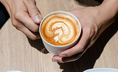 young man holding cup of coffee in hands on wooden background