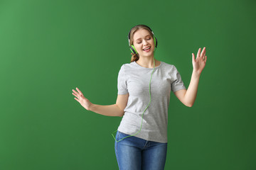 Beautiful young woman listening to music and dancing against color background