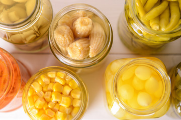 Jars with different canned vegetables on white table