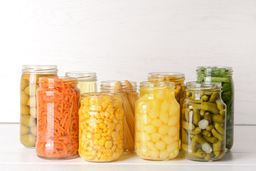 Jars with different canned vegetables on white table