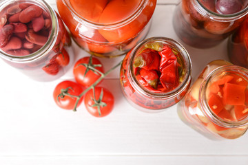 Jars with different canned vegetables and beans on white table