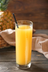 Glass of tasty pineapple juice on wooden table