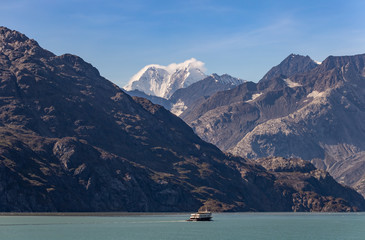 A fishing boat sailing in Alaska with huge mountains and snowy peak in the background