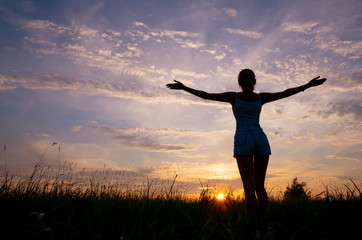 Silhouette of a girl on the background of the sunset sky and the sun, below - the grass. The concept of freedom, happiness, human unity with nature. Minimalism, a place for text.