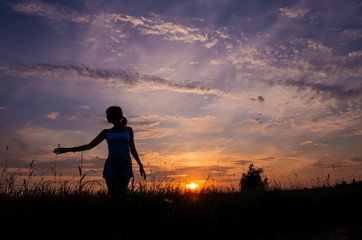 Silhouette of a girl on the background of the sunset sky and the sun, below - the grass. The concept of freedom, happiness, human unity with nature. Minimalism, a place for text.