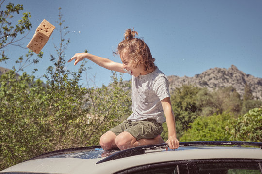 Side view of adorable child with sponge sitting on foamy glass roof of car and dropping sponge