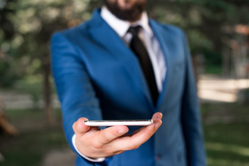 Businessman in blue suite stands with mobile phone in hands.