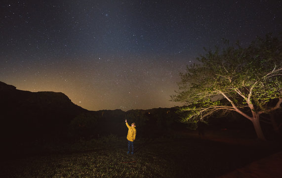 Boy in yellow jacket standing under the stars in dark night pointing to the sky