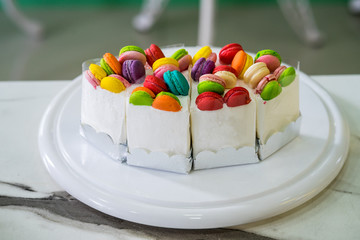 Cream cake decorated with macaron  on top, placed on a wooden plate