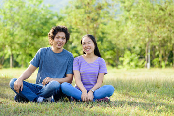 Naklejka na ściany i meble Happy Asian couple sitting on green grass in outdoor