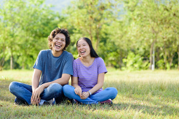 Fototapeta premium Happy Asian couple sitting and laughing on green grass in outdoor