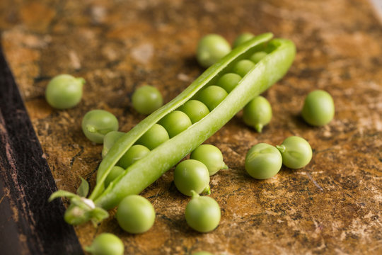 Peeled fresh peas and pea pods on dark background