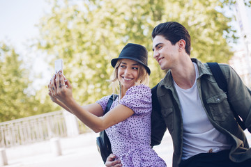 Young handsome man taking photo with girlfriend while walking in beautiful garden on background of historical building