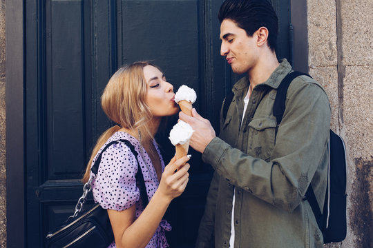 Cheerful young attractive woman and boyfriend eating cornet of ice cream outdoors