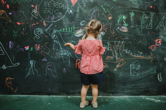 Back view of unrecognizable adorable child drawing at school during class in a writing green board
