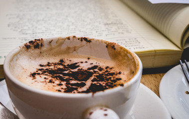 Cappuccino with chocolate dusting next to hand-written diary journal notes in cafe