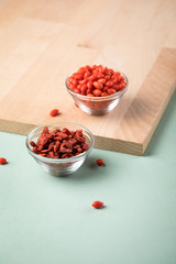 Frische und getrocknete Goji-Beeren Superfood in Glas Schale auf Holz Brett und Mint Grün Pastell...
