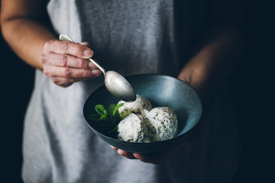 Crop view of anonymous woman with spoon in hand and holding bowl with stracciatella ice cream balls decorated with mint leaves