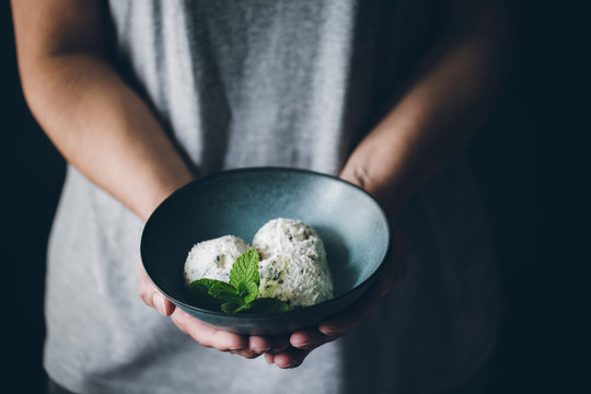 Crop view of anonymous woman holding bowl with stracciatella ice cream balls decorated with mint leaves