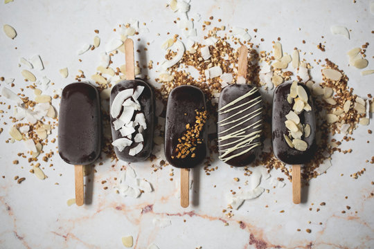 Top view of assorted chocolate ice cream popsicles covered with different toppings on a marble surface