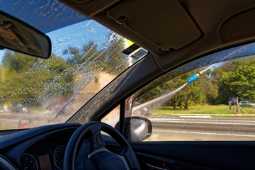 A car is being hand washed, the hose can be seen outside the driver's window