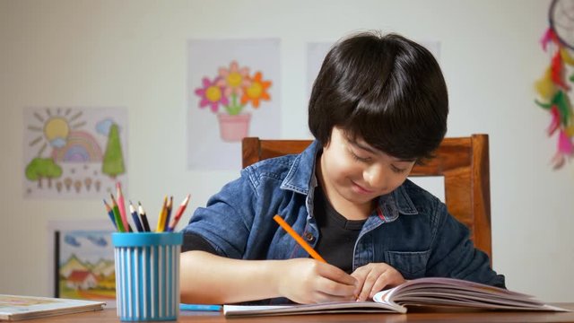 Talented Indian boy picking the color pencil to draw a picture - Education in Childhood. Little boy completing his art homework with the bight color shading pencil - child concept
