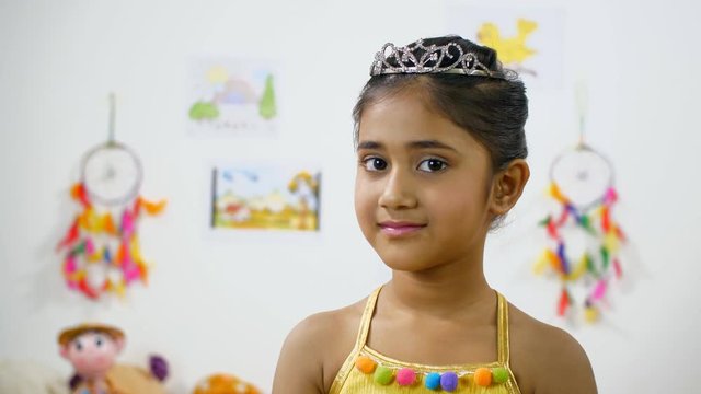 Indian girl with a smile on her face posing at  camera - Colorful background 
. Cute little princess with a crown on her head - looking towards the camera