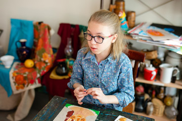 Fototapeta premium Smiling pretty blonde girl enjoying their time at art studio. close up photo. Sculpting lessons. little girl makes a nice pportrait