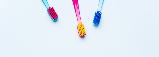 Colorful tooth brushes with bright color bristles on a light pastel blue background. Long wide...