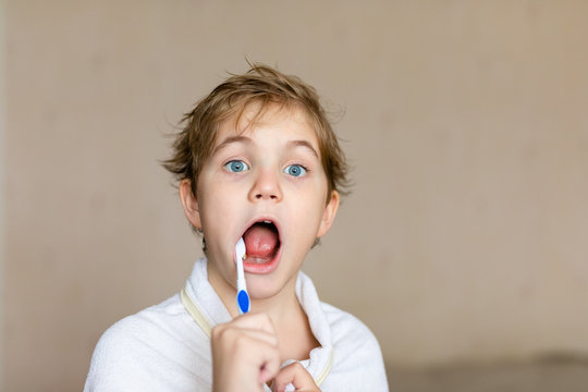 A cute little blonde boy with blue eyes brushing his teeth with a toothbrush. The concept of children's health, medicine