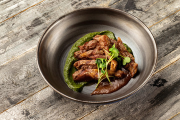 Pan of baked duck breast served with sauces at rustic wooden table background.
