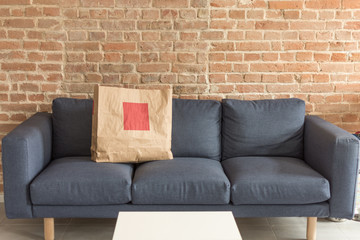 Blank paper gift or shopping bag standing on blue modern sofa. Empty paper package for mockup on modern living room interior.