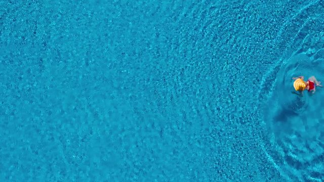View from the top as a woman in a red swimsuit and a big yellow hat swims in the pool