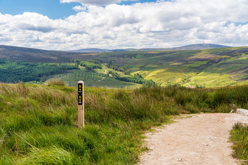 Irish mountain landscape with a hiking path and a trail marker. Scenery in Wicklow Mountains, Ireland with green rolling hills under the summer sun. © Gabriel