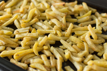 Oven baked potato sticks. French fries on dark baking tray top view. Fast food potato skins on a baking tray. Seasoned potato sticks.