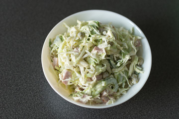 Salad with cabbage and mayonnaise in a bowl top view on black background. Spring salad with cabbage.
