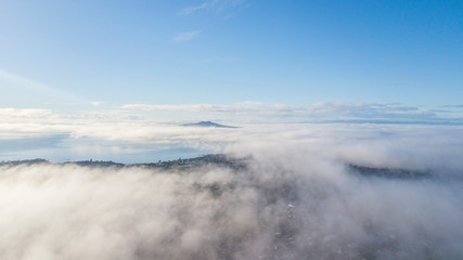 Aerial drone shot flying above the cloud, looking at the summit of Rangitoto Island.